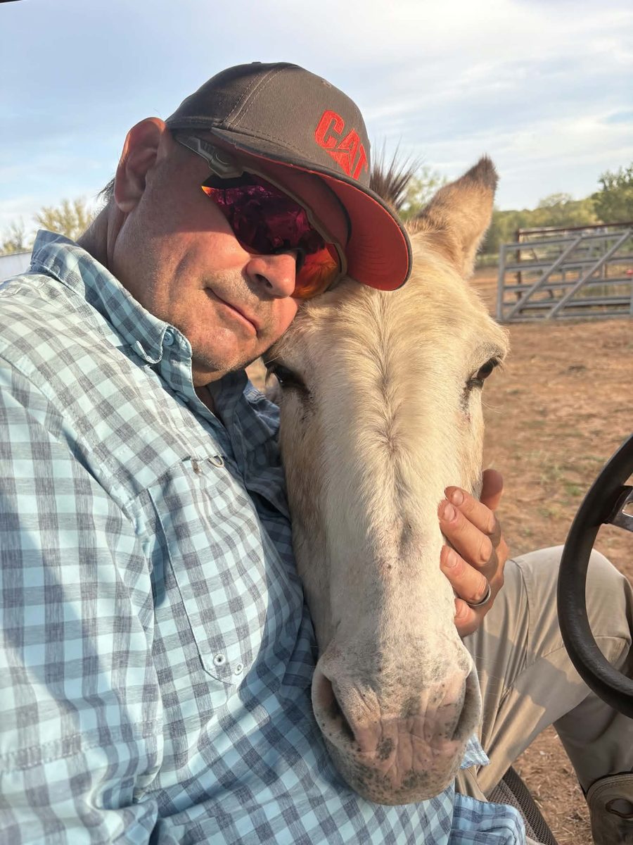 A man leaning cheek to nose with one of the ranch donkeys, early morning light
