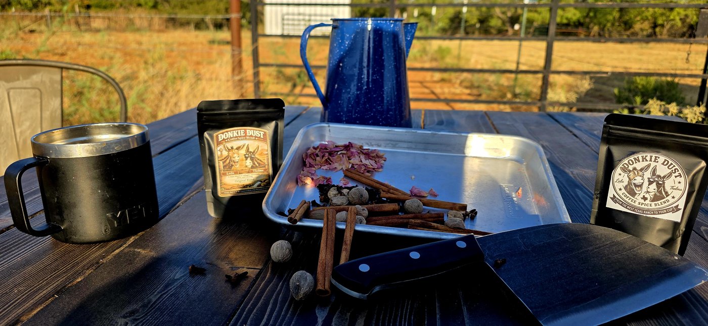 The full Donkie Dust lineup laid out on the ranch table, mug, pouches, coffee pot, and fresh-cut spices, one evening this week